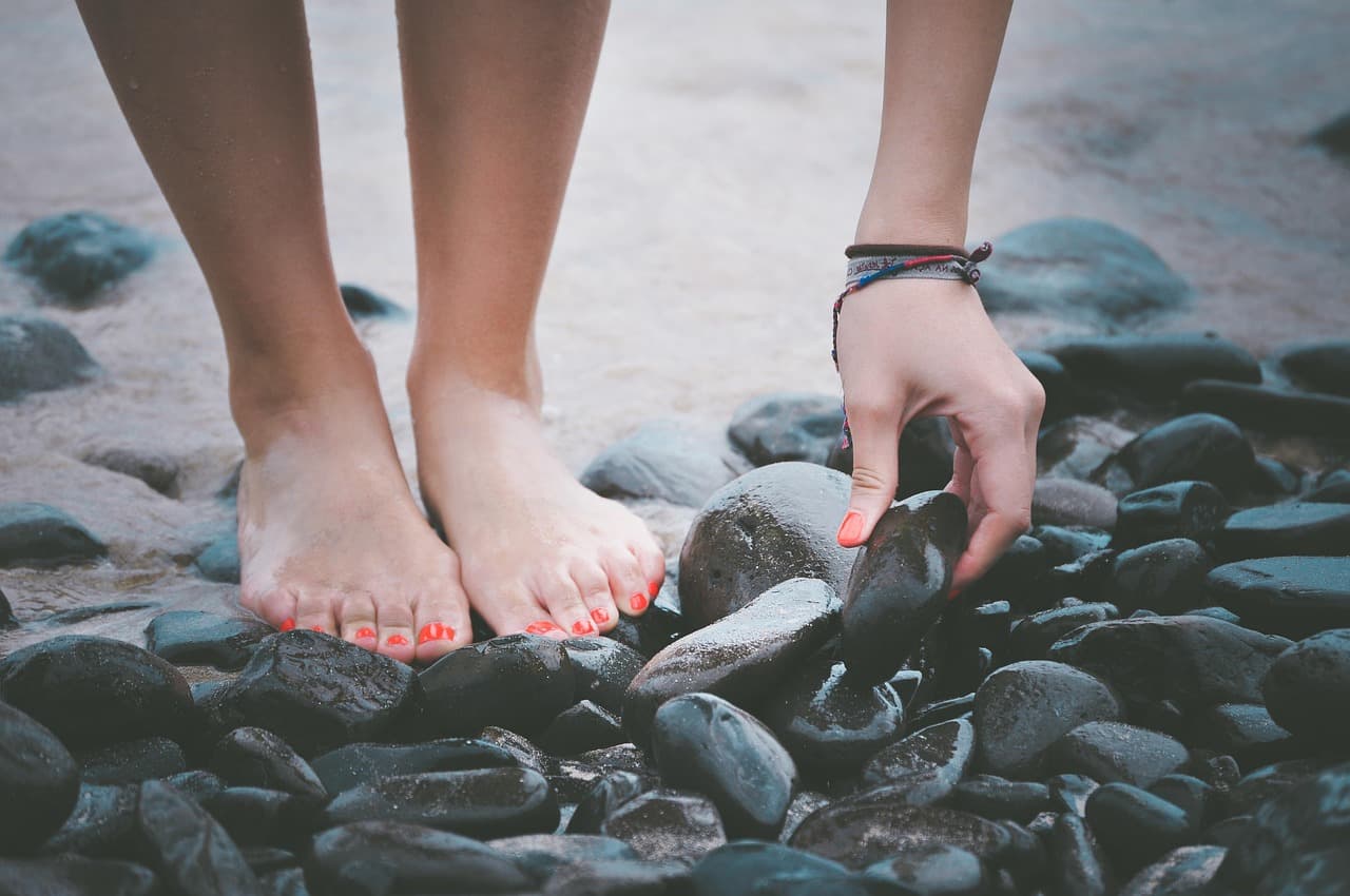 Bare feet with coral toenails standing on dark, smooth pebbles